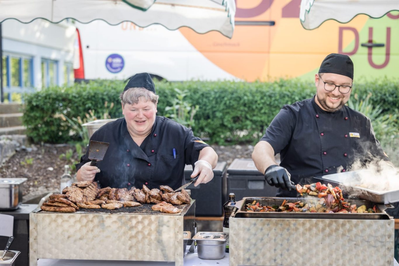 Zwei Köche grillen Fleisch und Gemüse an einem Straßenfest.